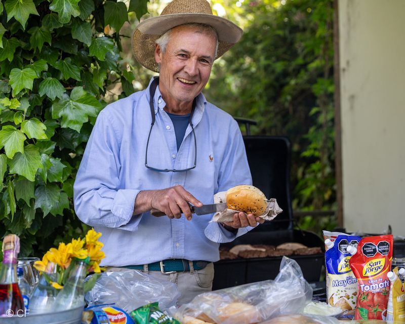 A man in a hat is cutting a hamburger on a bun.