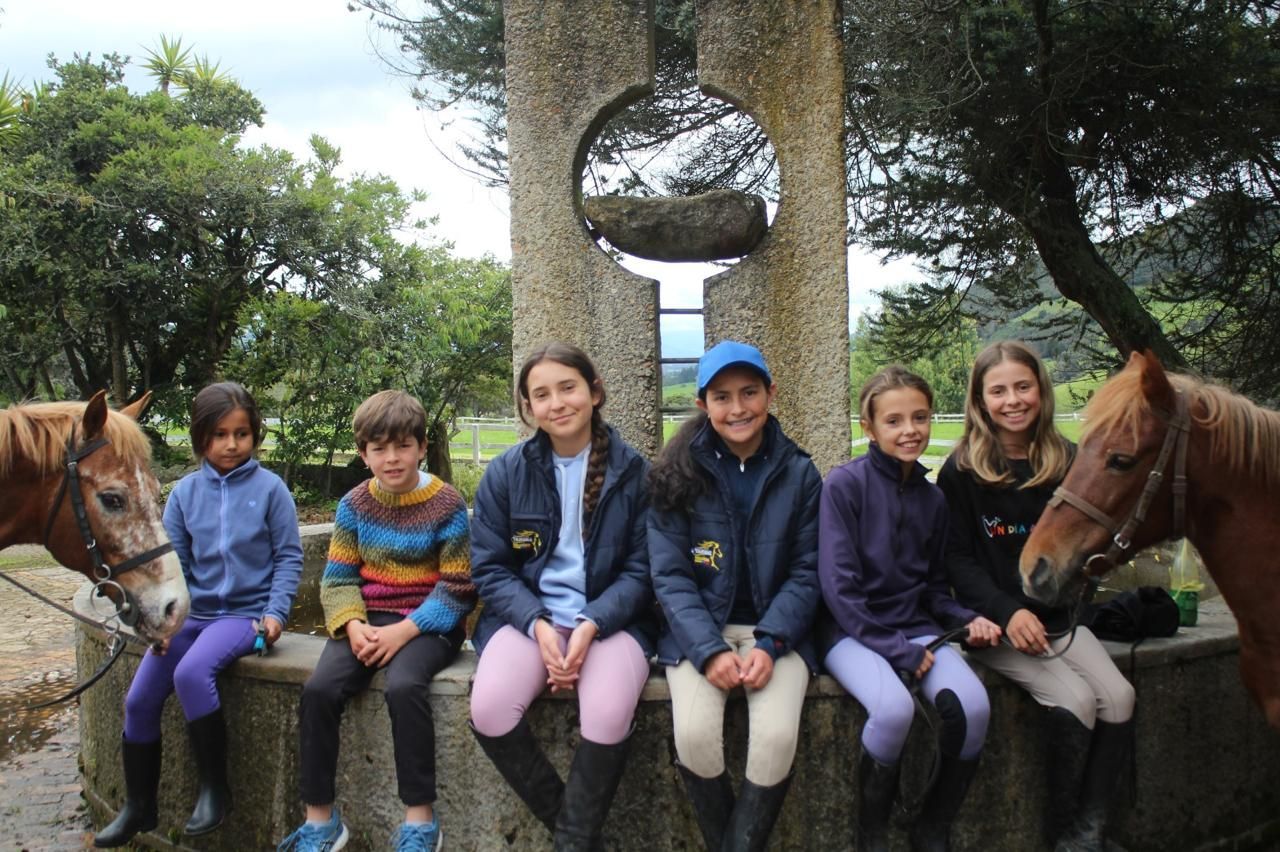A group of young girls sitting on a stone wall next to horses