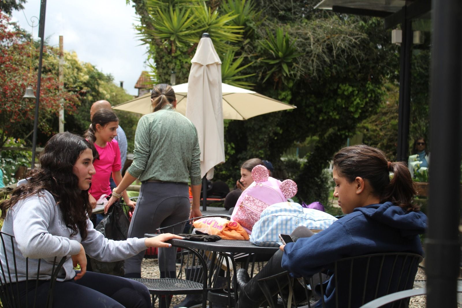 A group of people are sitting at tables outside under umbrellas.