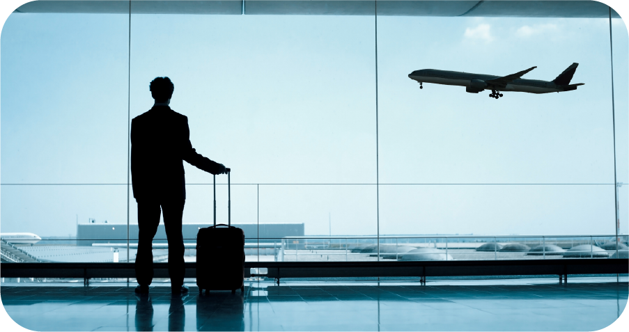 A man with a suitcase is looking out a window at an airplane taking off