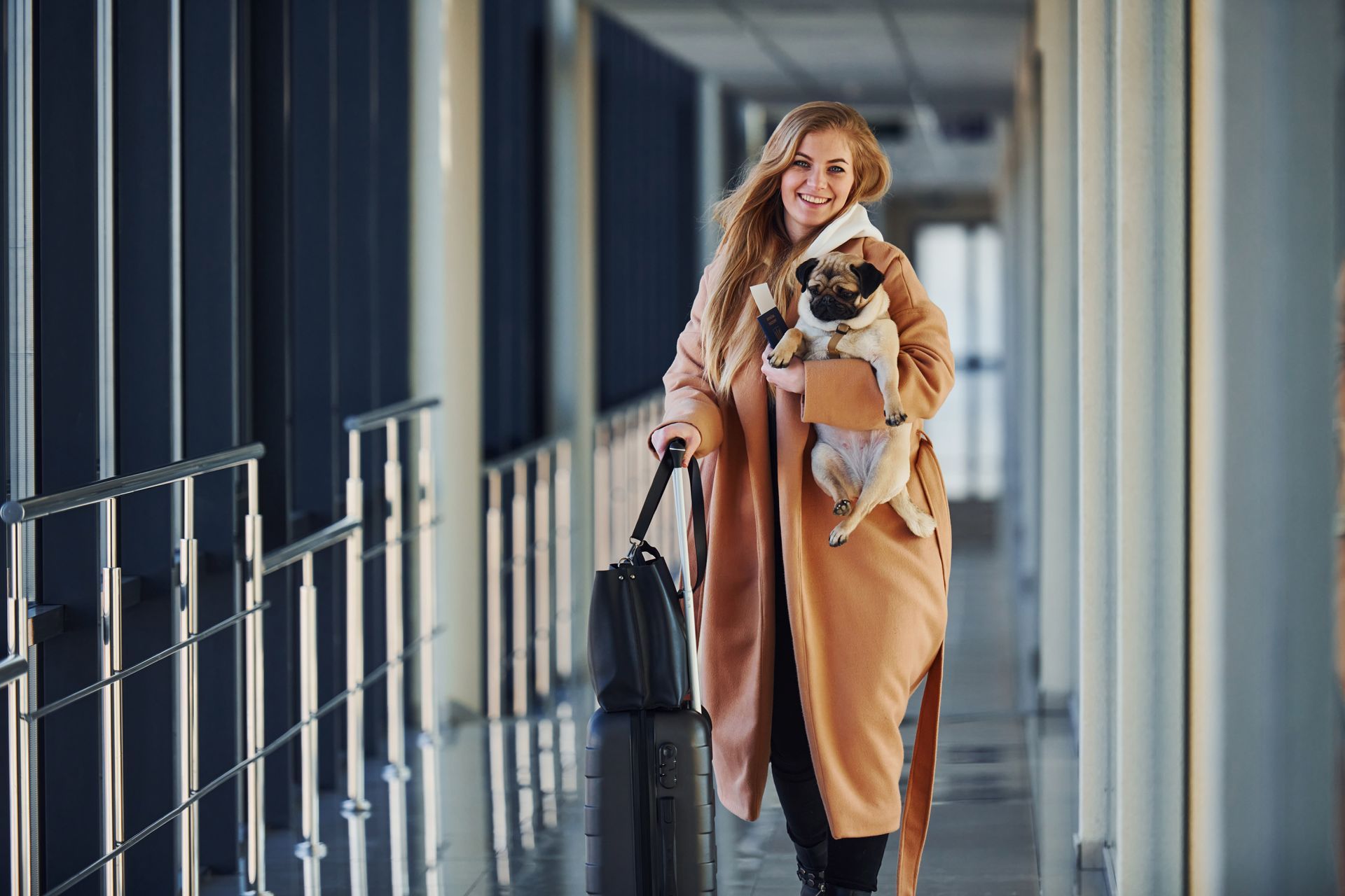 A woman is walking with a suitcase and a dog in her arms.