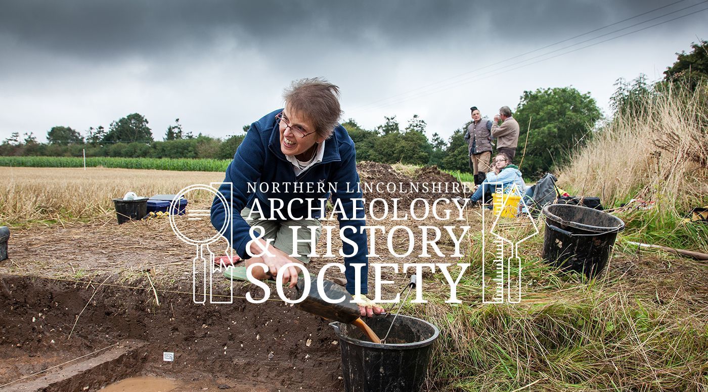 A woman is kneeling down in a field holding a shovel and pouring dirt into a bucket.
