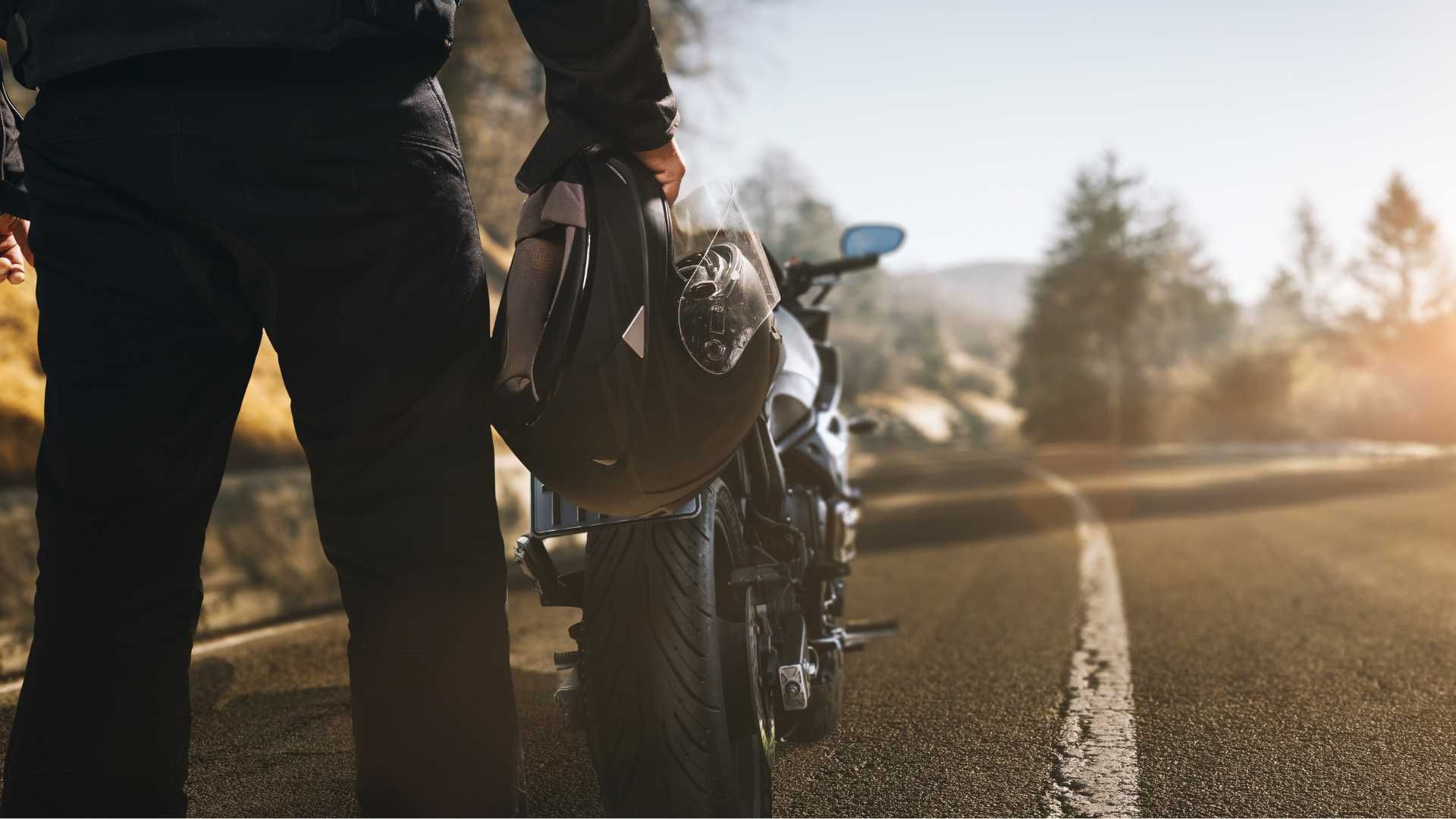 A man is standing next to a motorcycle holding a helmet.