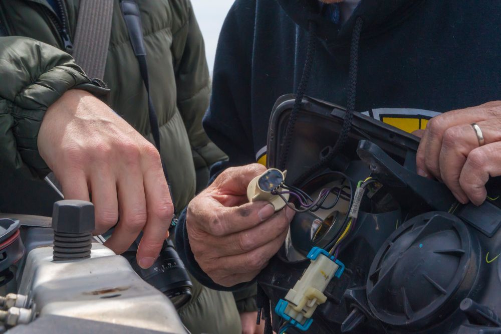 Two People Working on a Car Headlight, Holding Wires and a Connector — A.M.D. Automotive Services in Marian, QLD