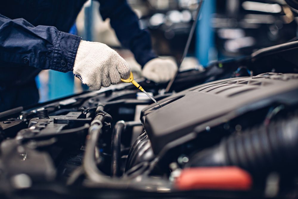 Mechanic in Gloves Checking Engine Oil With Dipstick in a Car Bay — A.M.D. Automotive Services in Mackay, QLD