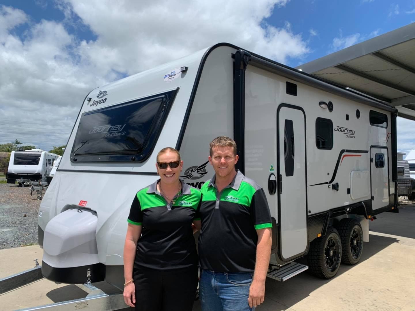 Couple Posing With a White Travel Trailer Under a Partly Cloudy Sky — A.M.D. Automotive Services in Mackay, QLD