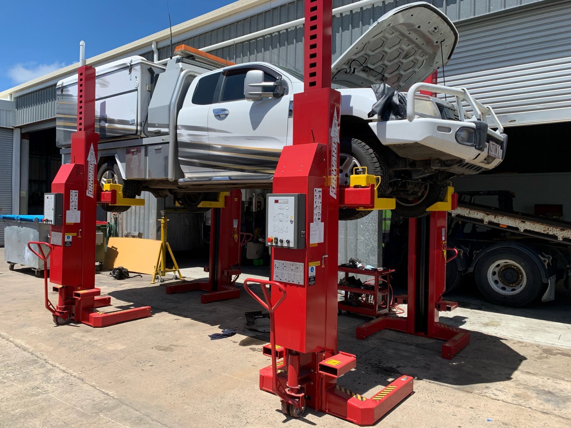 White Pickup Truck Raised on Four Red Hydraulic Vehicle Lifts in a Garage — A.M.D. Automotive Services in Mackay, QLD