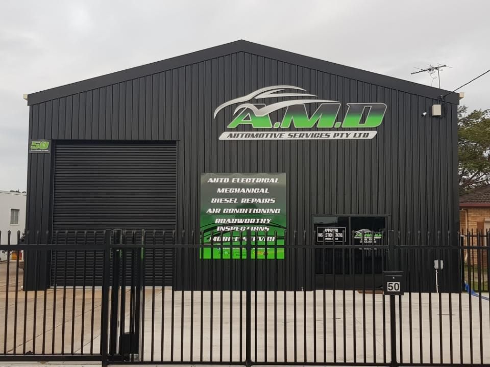 A dark metal warehouse building with green A.M.D. Automotive Services signage and an auto repair service list on the front — A.M.D. Automotive Services in Mackay, QLD