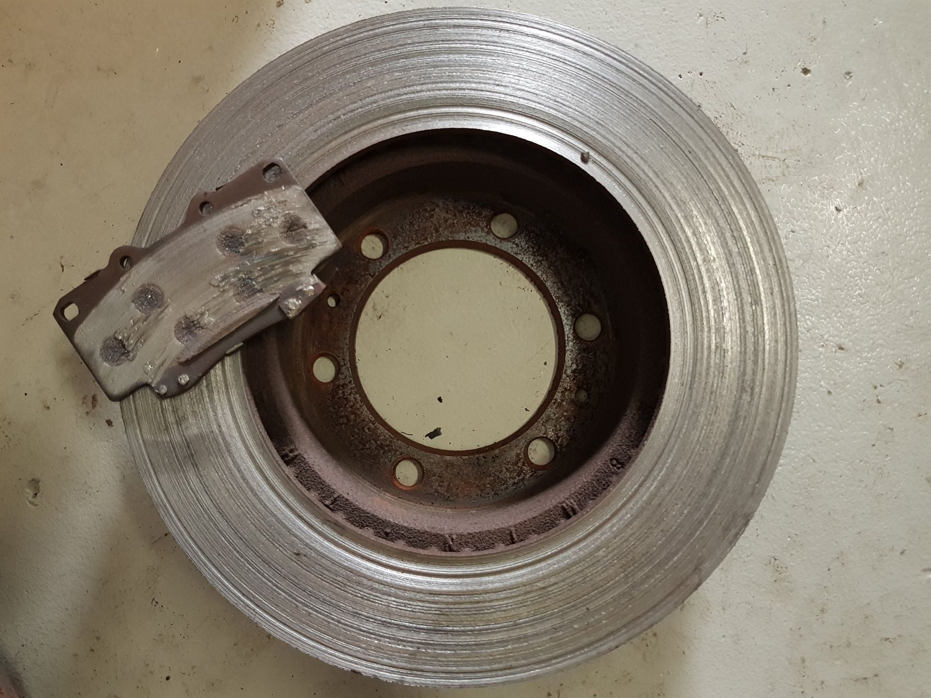 Brake Rotor and Pad, Worn and Rusty, on a White Surface — A.M.D. Automotive Services in Mackay, QLD