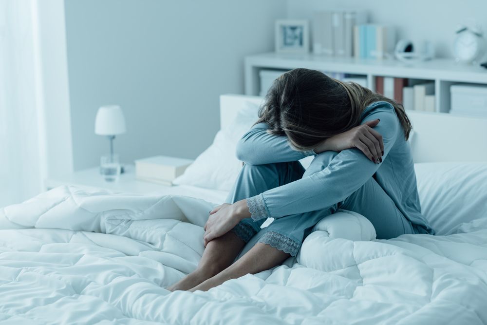 A woman is sitting on a bed with her head in her hands.