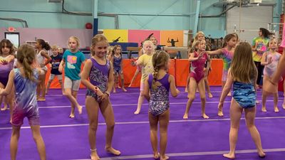 A group of young girls are dancing on a purple mat in a gym.