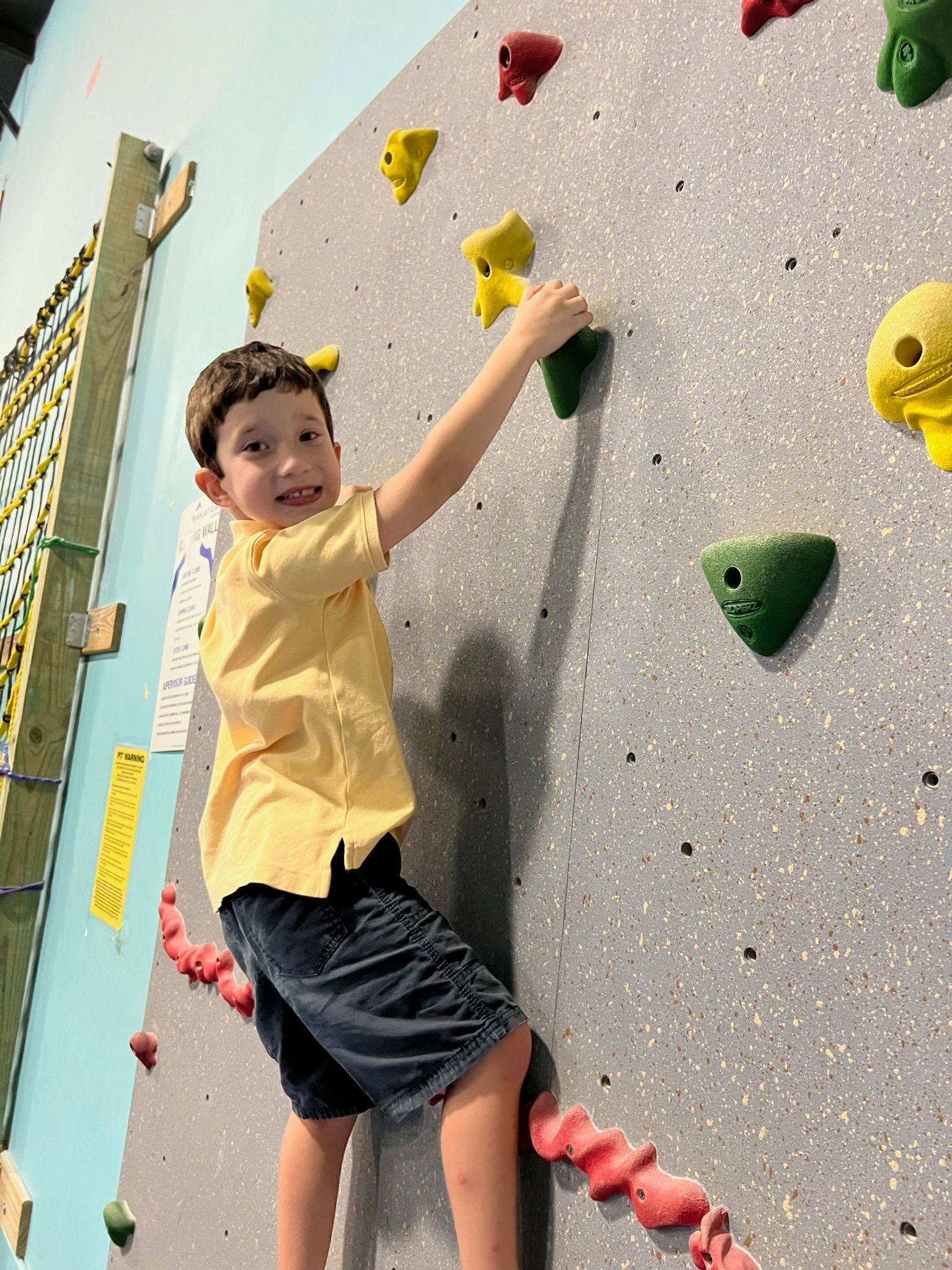 A young boy is climbing up a climbing wall