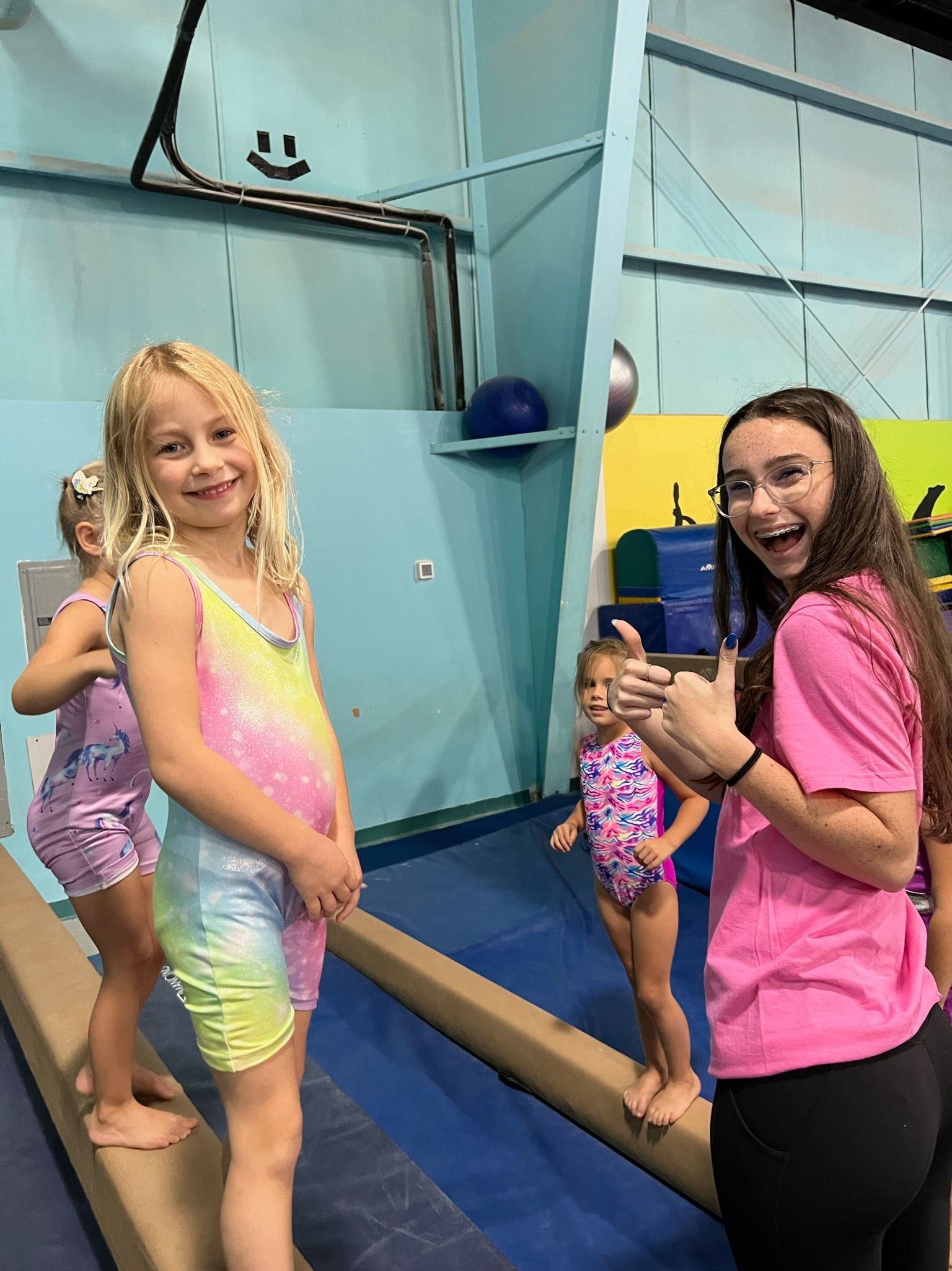 A group of young girls are standing on a balance beam in a gym.