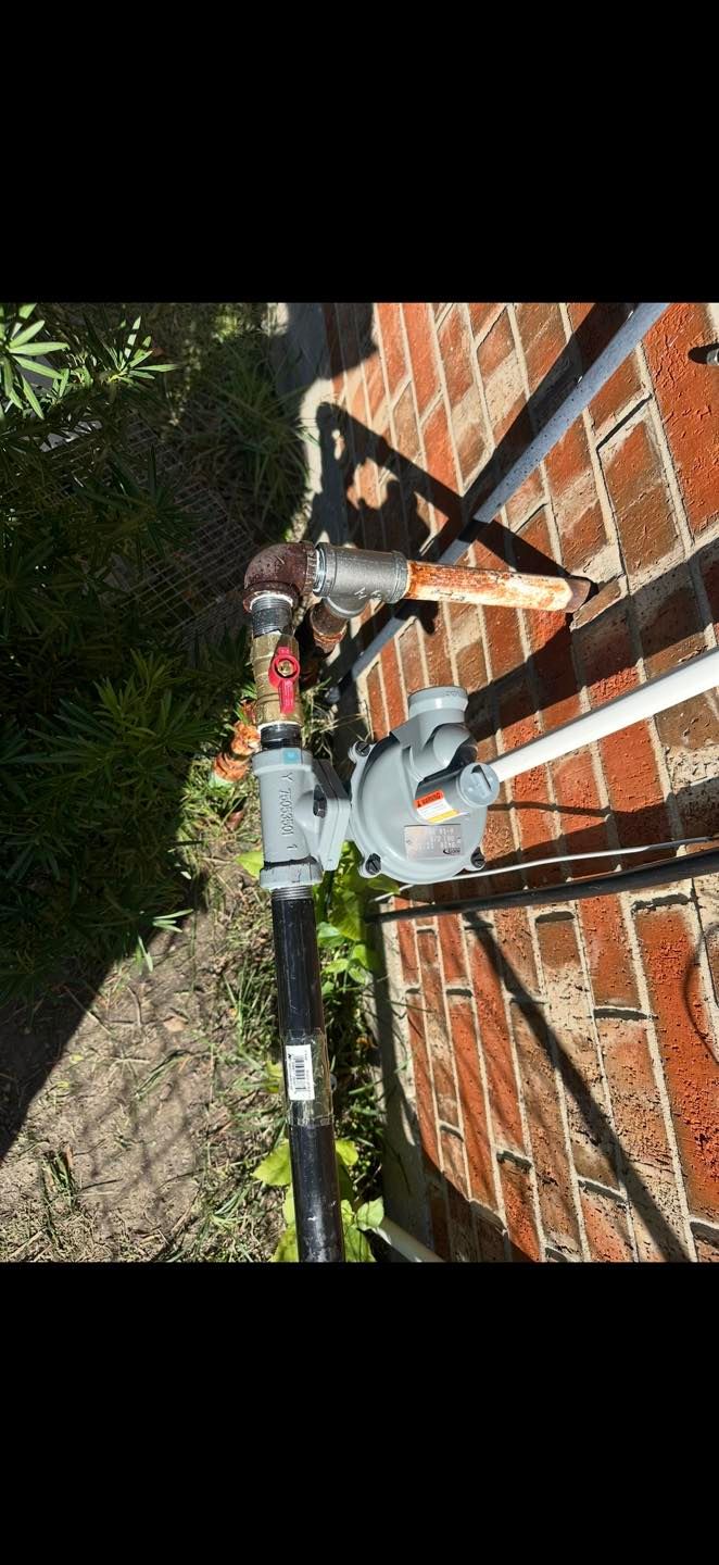 Two gray utility pumps mounted on a brick wall beside a walkway and greenery