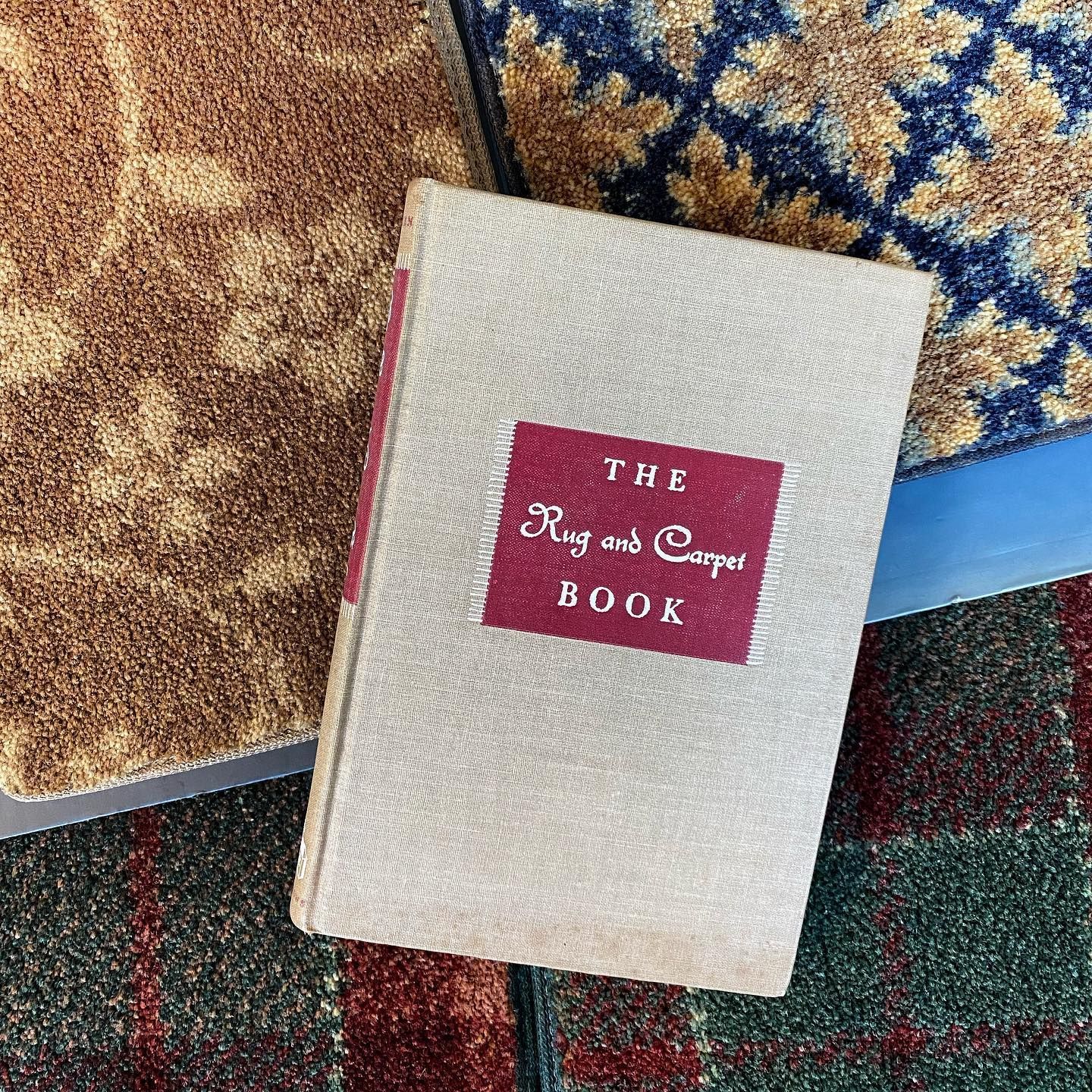 A book titled the rug and carpet book is sitting on a carpet