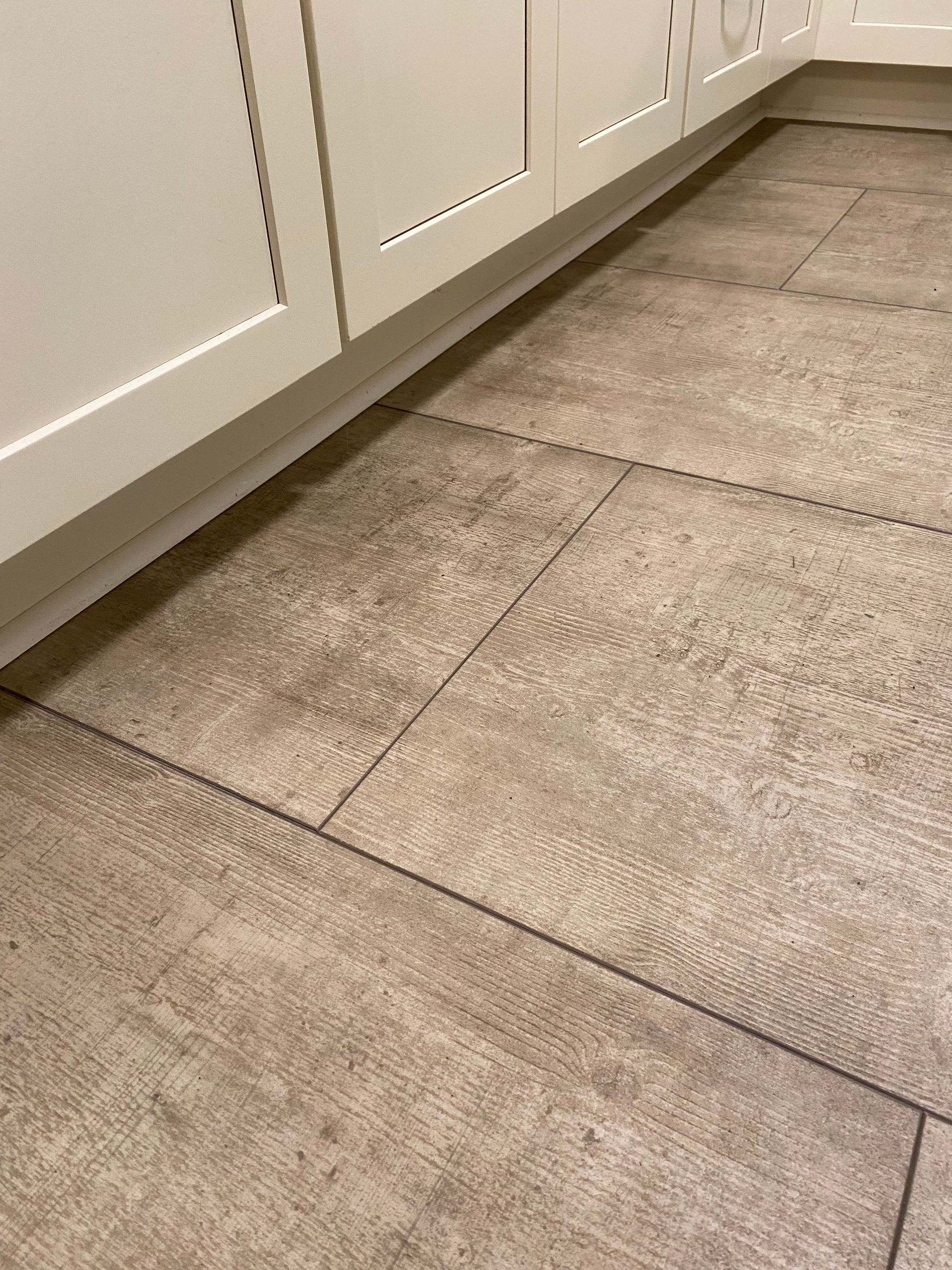 A close up of a tile floor in a kitchen with white cabinets.