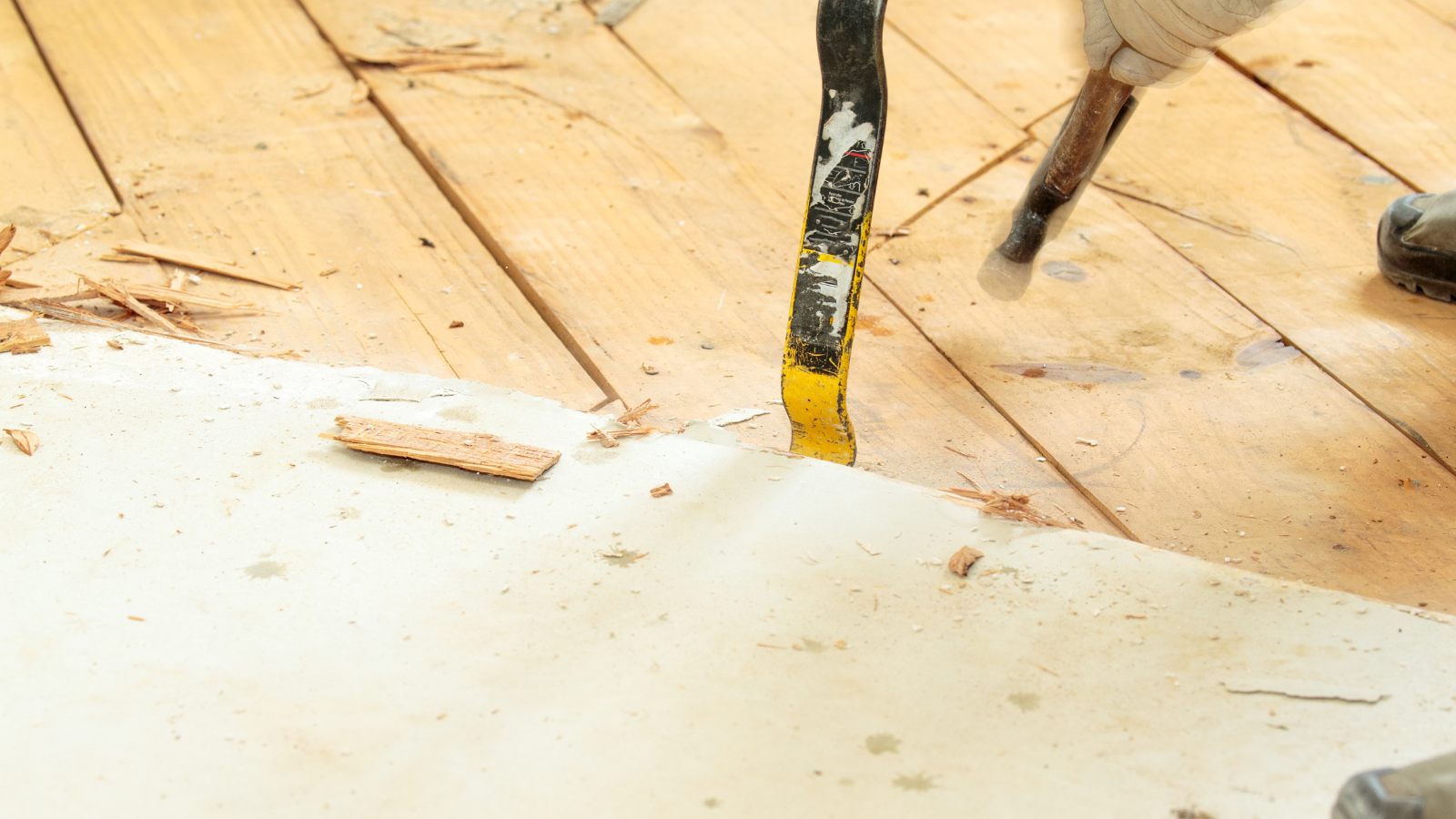 A person is using a spatula to remove wallpaper from a wooden floor.