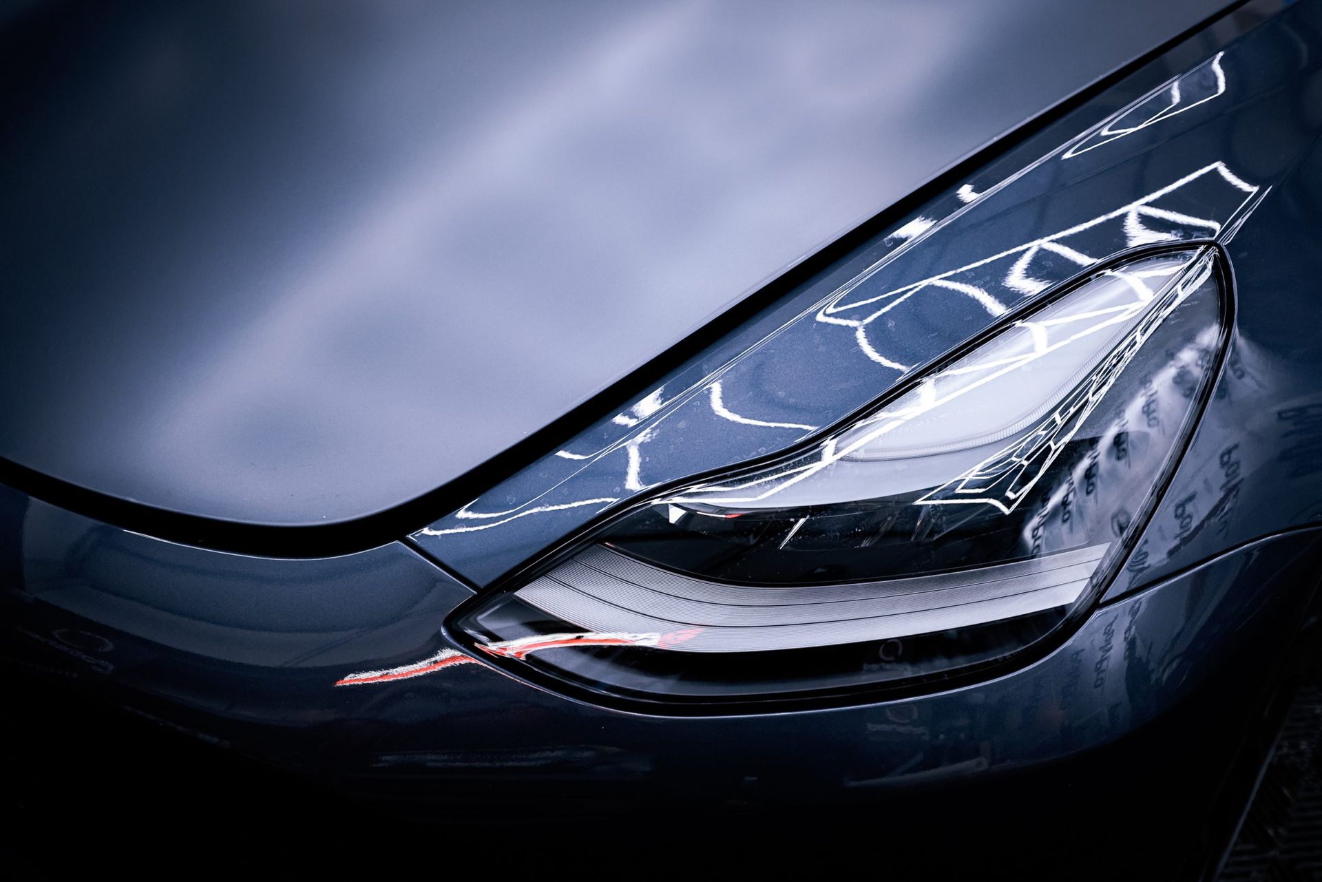 A close-up, angled view of a sleek, dark blue car's LED headlight and hood with studio lighting reflections.