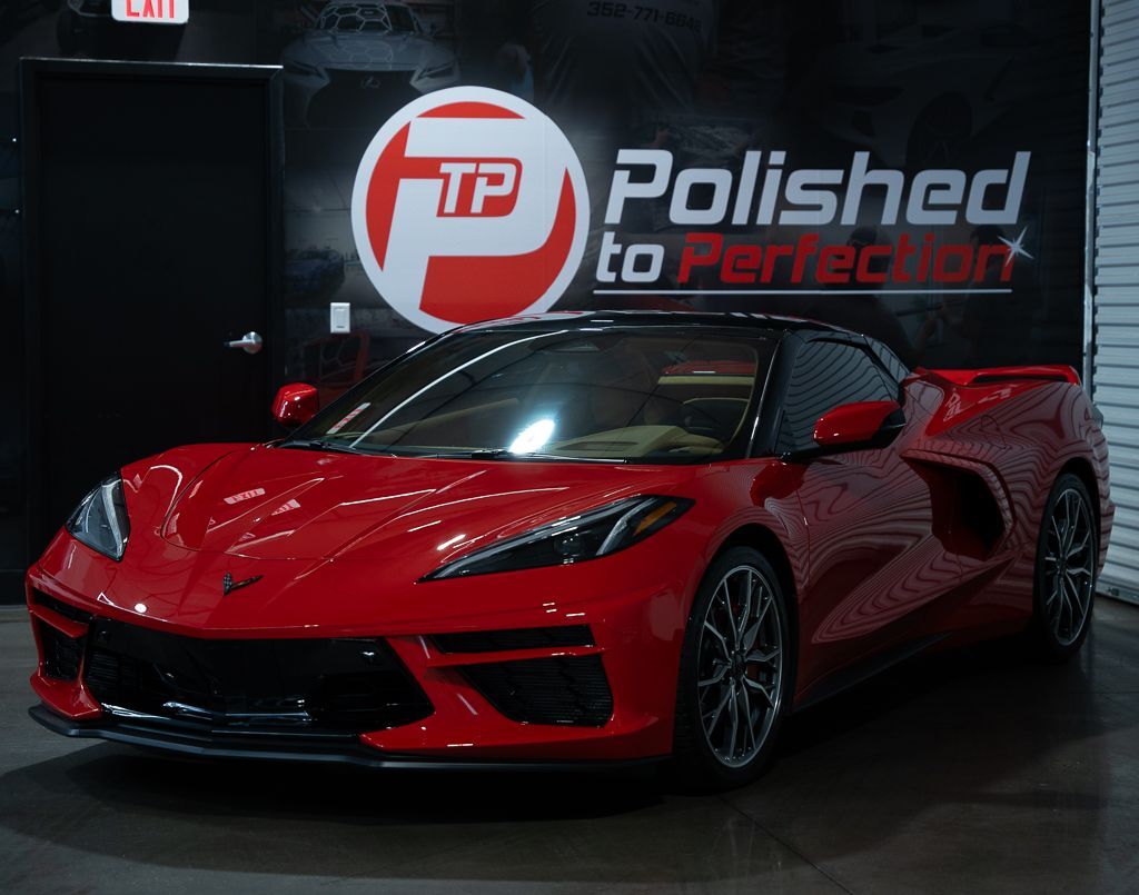 A gray Porsche Cayman parked on an asphalt lot in front of a metal warehouse building.