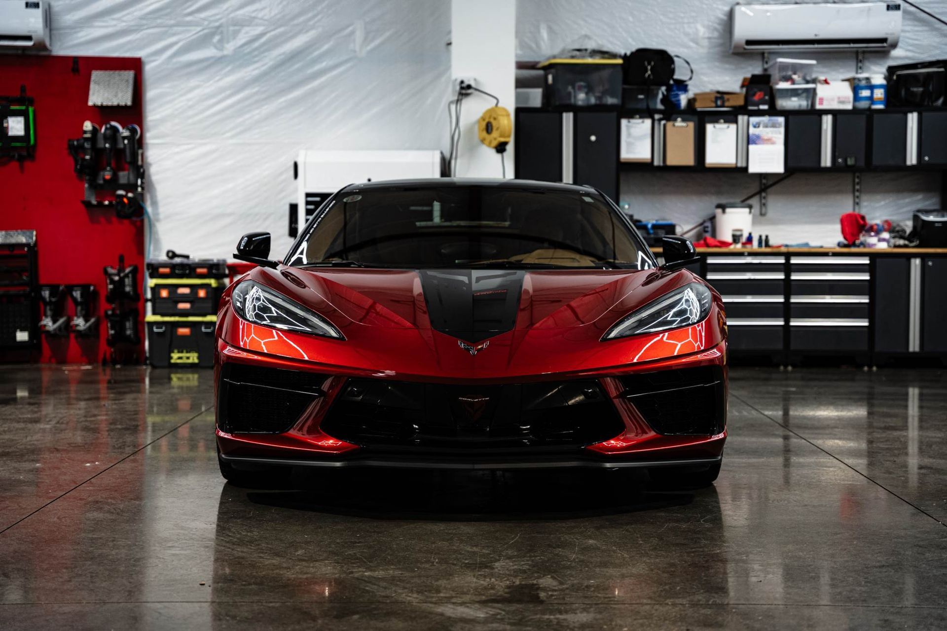 A shiny, metallic red Chevrolet Corvette sits centered in a clean, well-lit professional automotive garage.