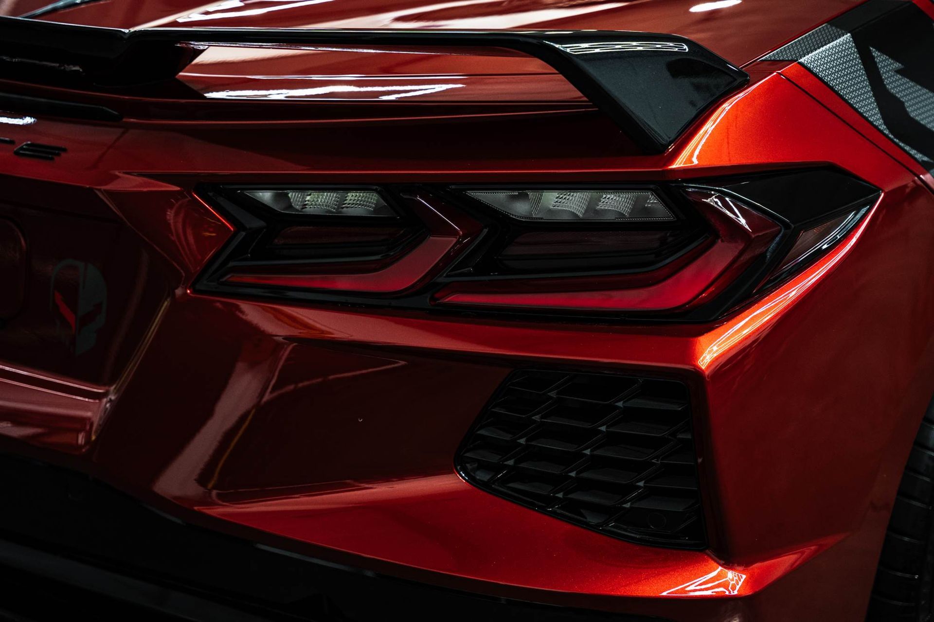 Close-up of the rear taillight, spoiler, and air vent of a metallic red Chevrolet Corvette C8 sports car.