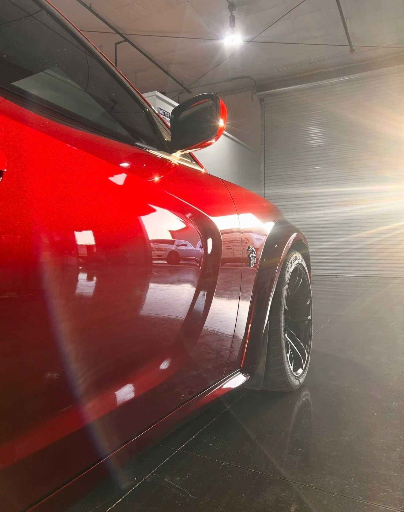 A low-angle view of a shiny, bright red sports car parked in a garage with a prominent wheel flare and black alloy wheels.