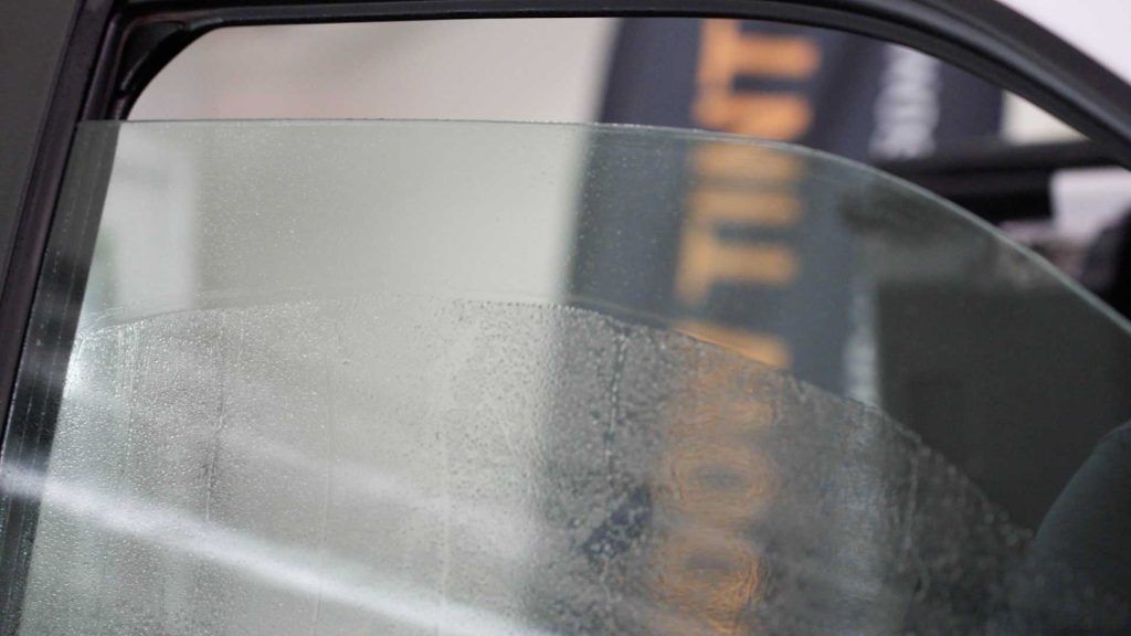 A car window being sprayed with water during the process of applying window tint film.