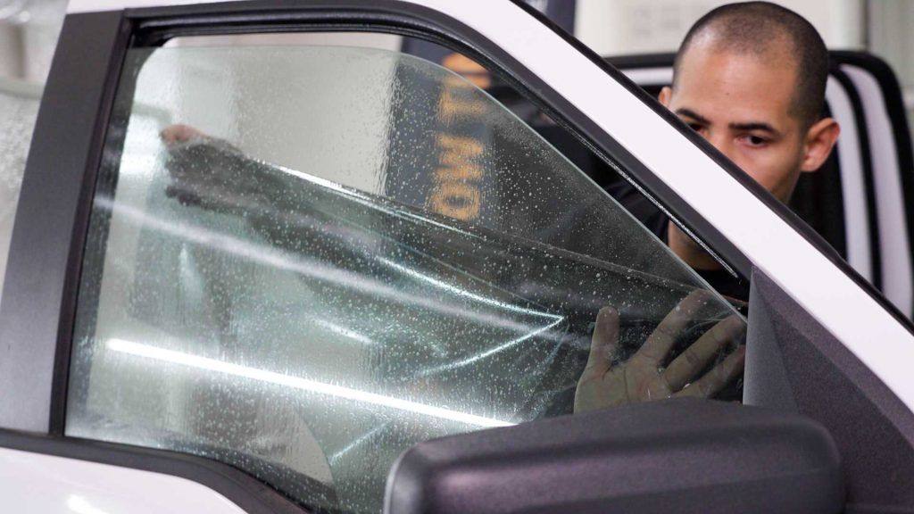 A technician carefully applies window tint film to a car door window using a squeegee to remove air bubbles.