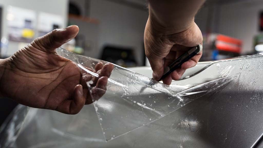 A man is applying a protective film to the headlights of a mercedes benz.