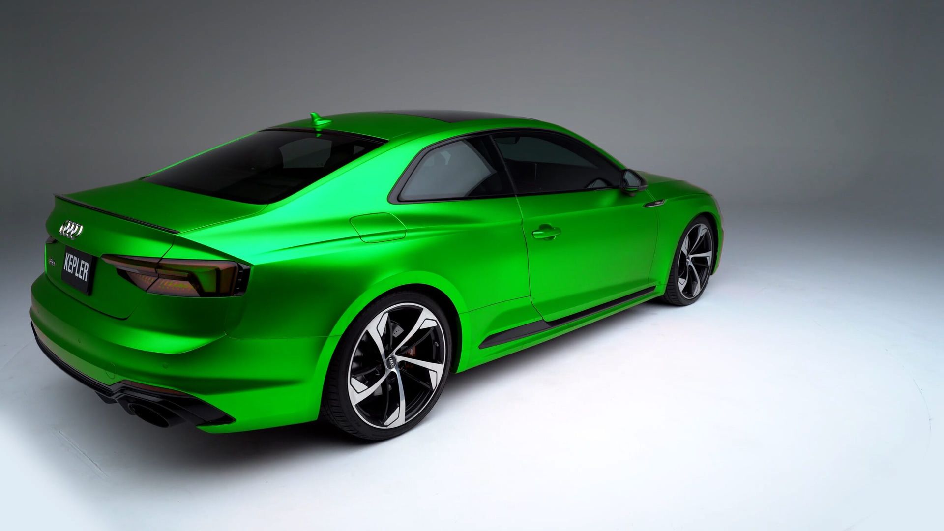 A bright green Audi coupe viewed from the rear three-quarter angle against a plain, light grey studio background.
