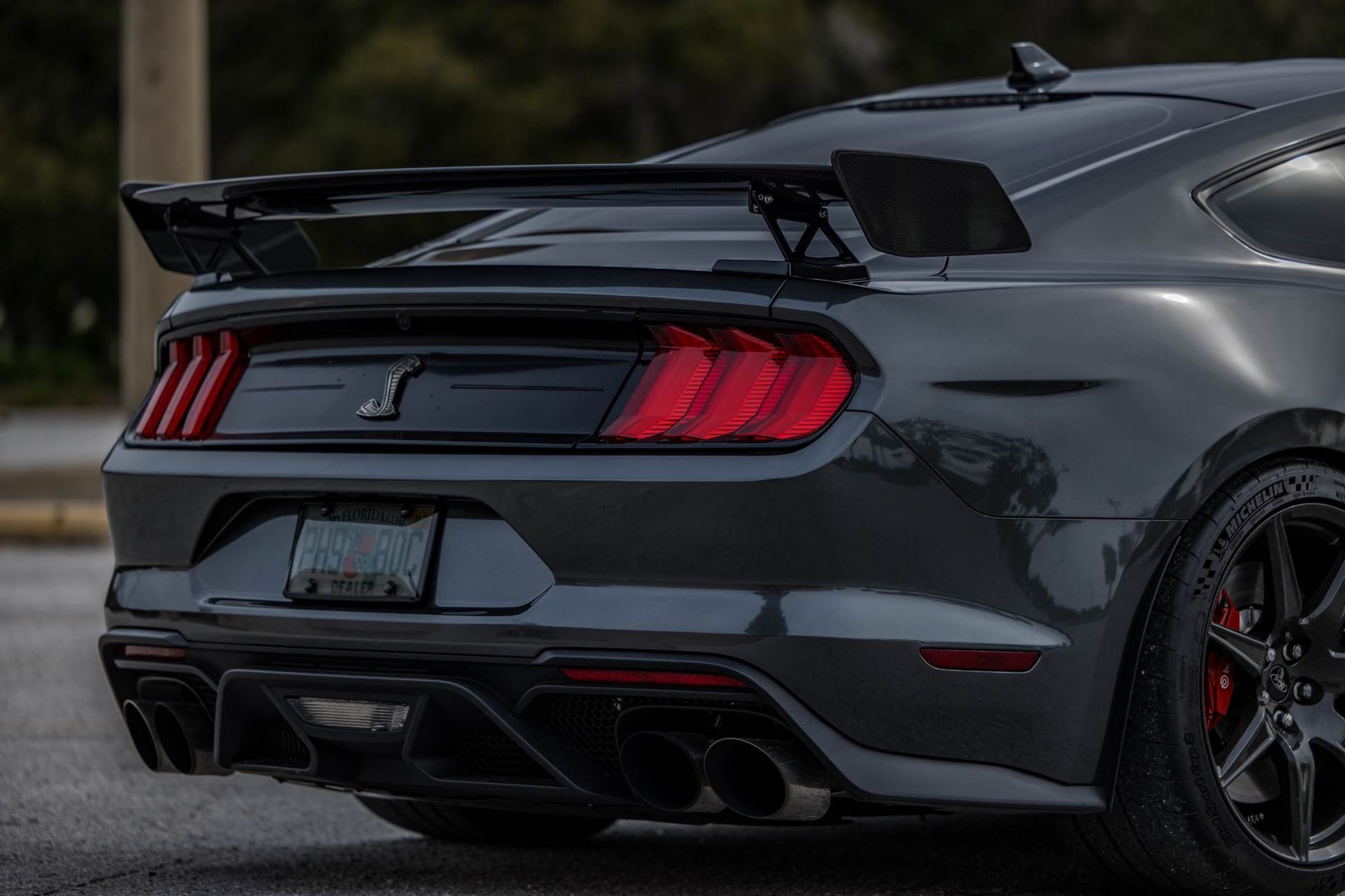 Rear view of a dark gray Ford Mustang Shelby GT500 with a large rear wing, quad exhaust tips, and a black diffuser.