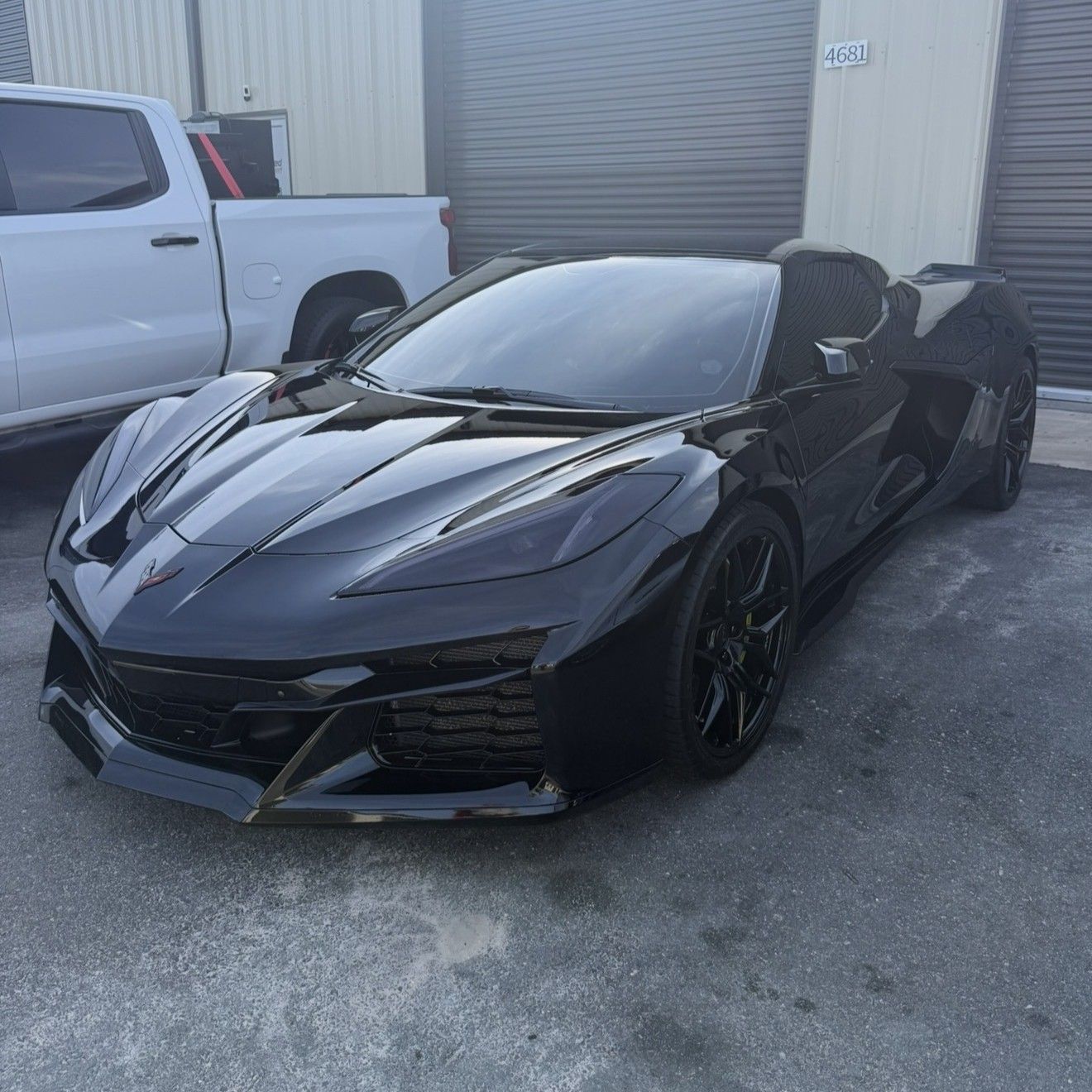 A black Chevrolet Corvette C8 Z06 parked on asphalt next to a white pickup truck.