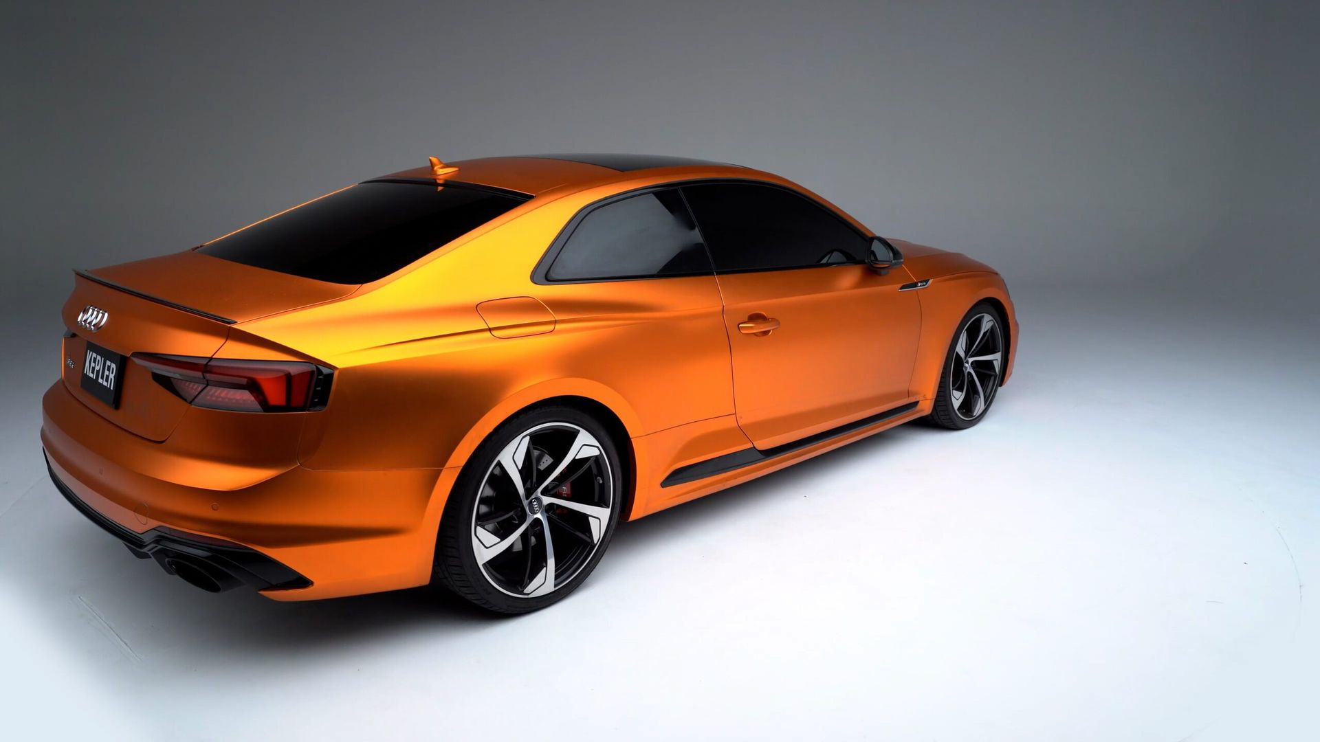A sleek, metallic orange two-door coupe car parked against a plain white studio background.