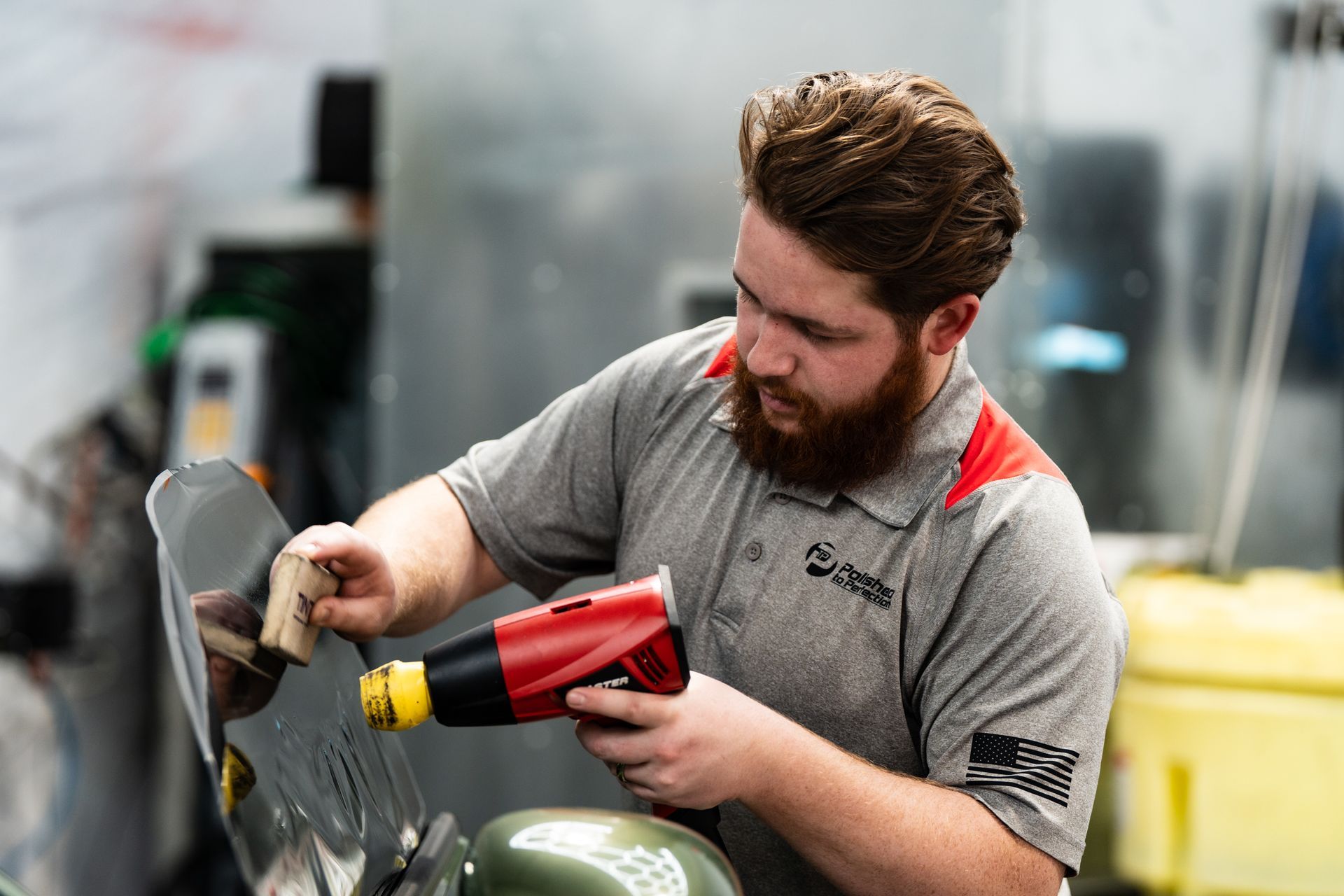 A person uses a thin metal tool to apply dark, wet window tint film to a glass surface.