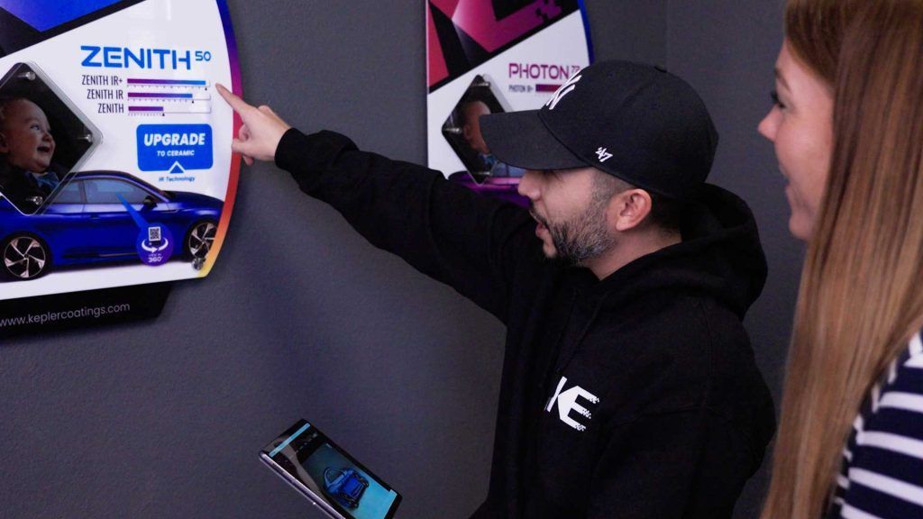 A person in a black hoodie and cap points to a Zenith vehicle display while talking to another person in a store.