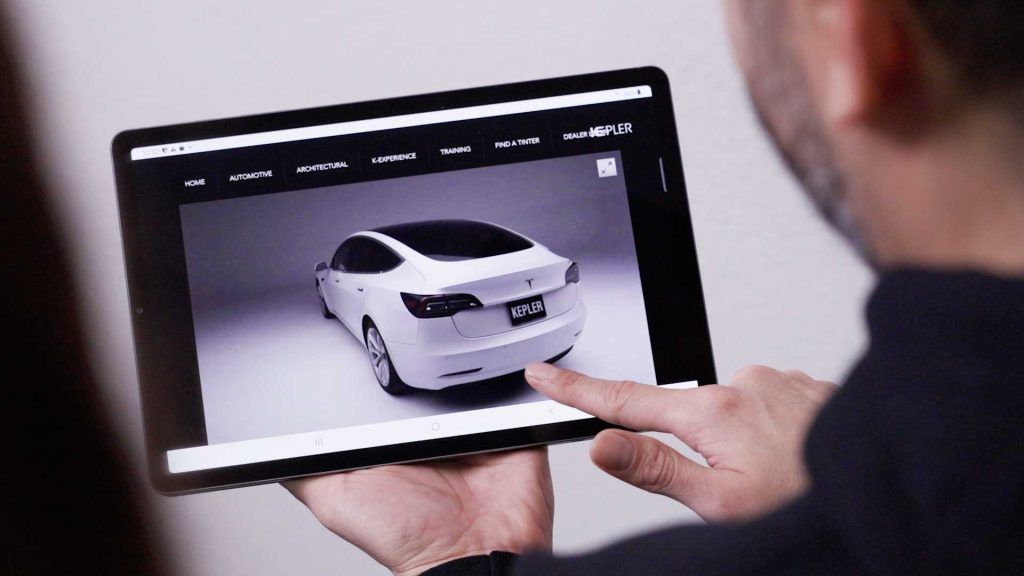A person interacts with a tablet showing a white car on a website.