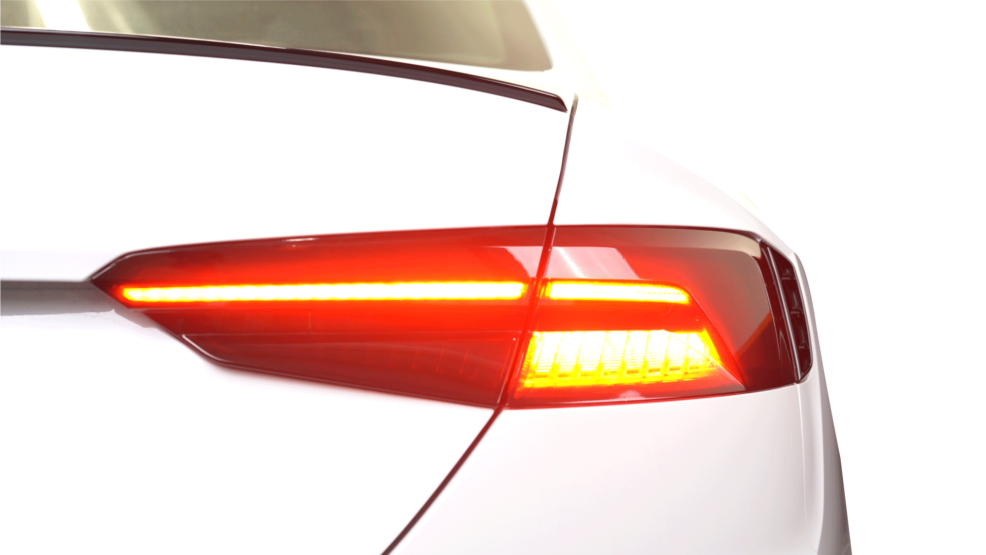 Close-up of a sleek white car's illuminated red LED taillight against a white background.
