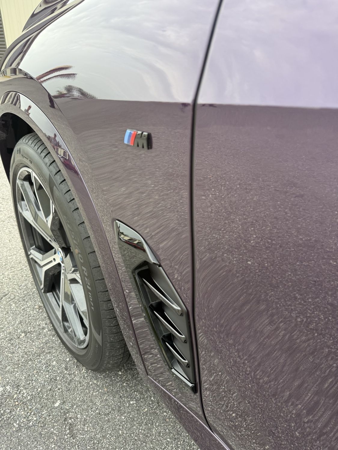 Close-up of front fender and side vent on a purple BMW X5 showing paint protection film wrapped behind the trim with no visible edge