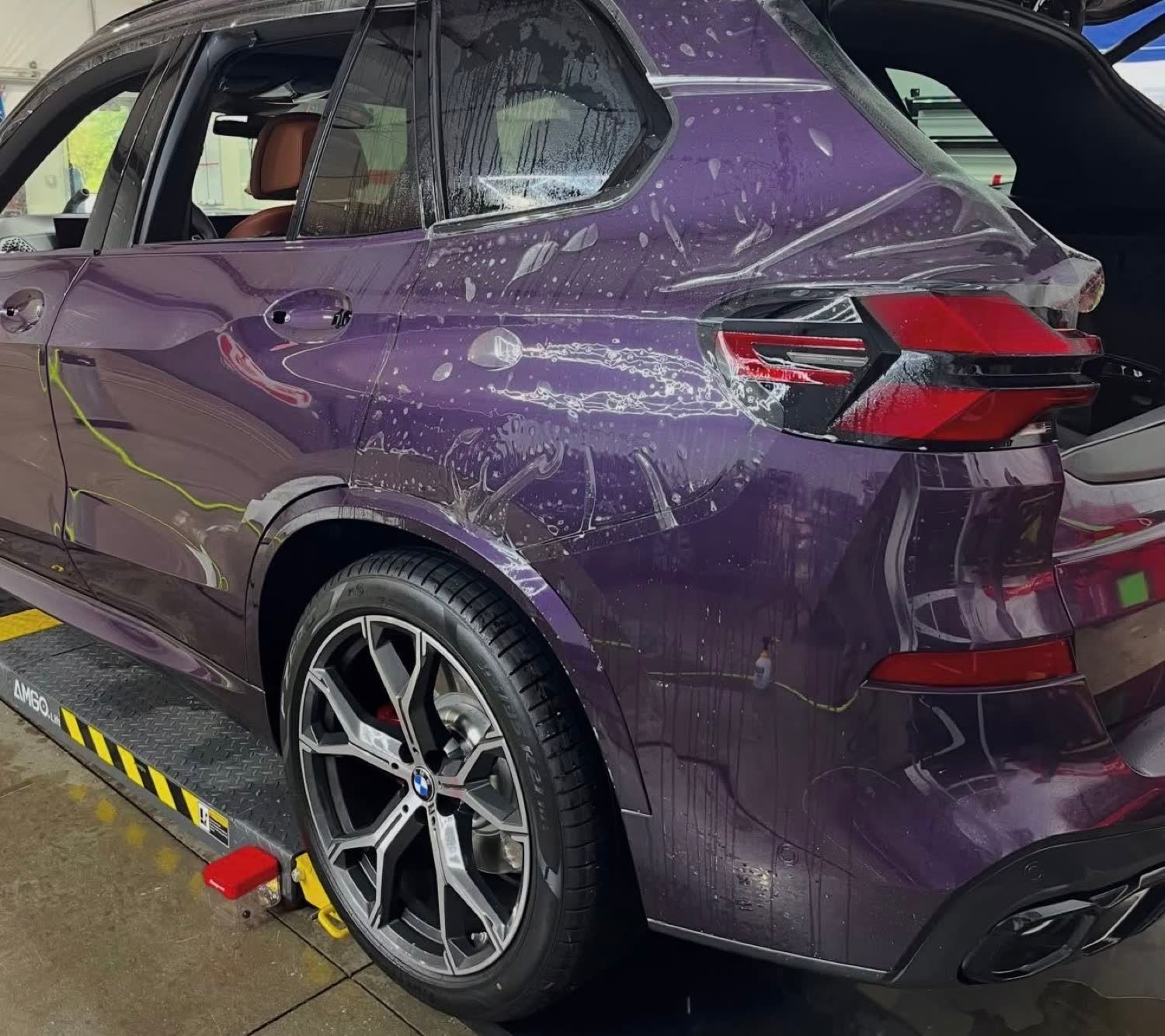 2026 BMW X5 on the lift mid-install with door handles removed and paint protection film laid over the rear quarter panel