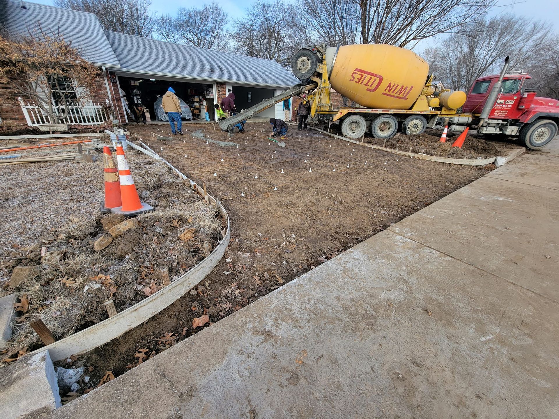 A concrete mixer truck is pouring concrete into a driveway in front of a house.