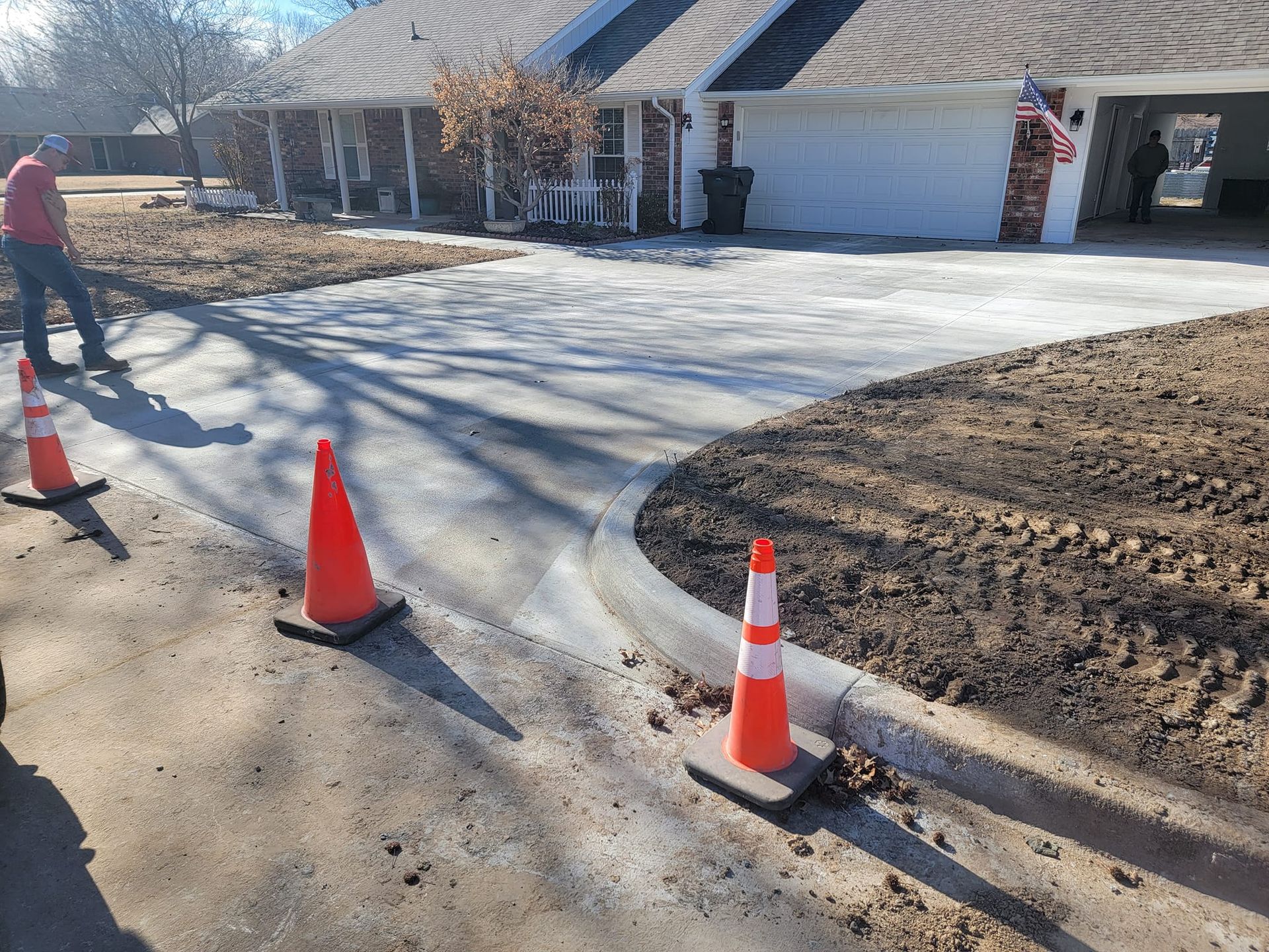 A man is standing next to a row of orange and white traffic cones on the side of a road.