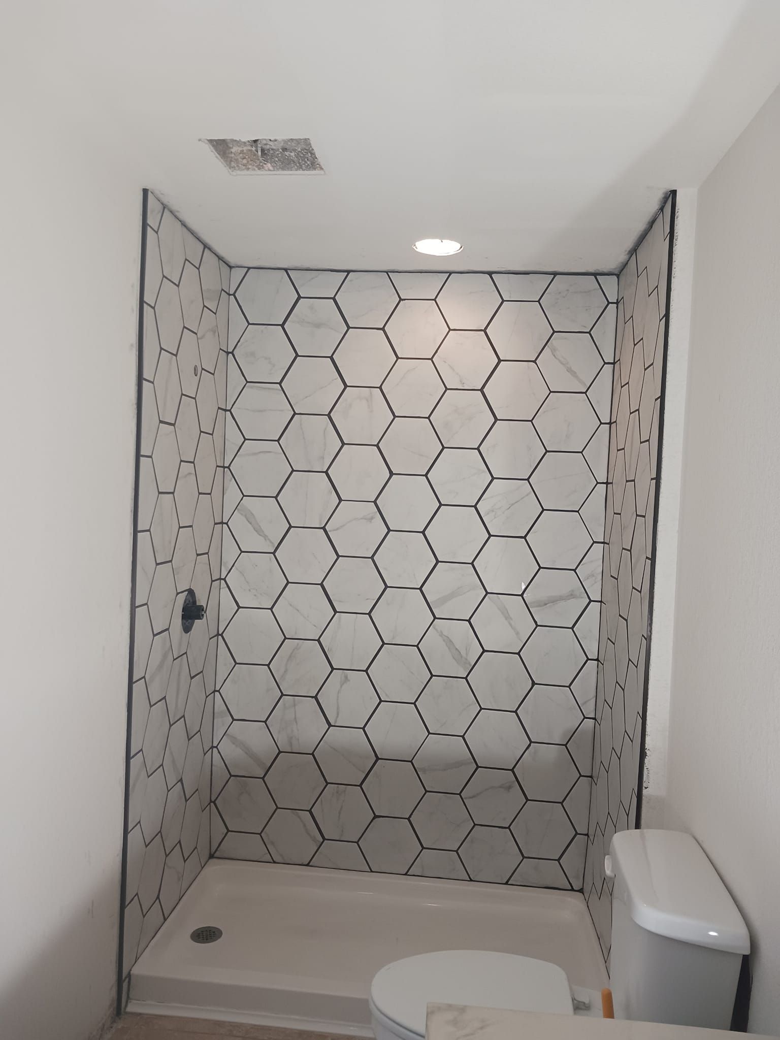A bathroom with a toilet and a shower with hexagonal tiles