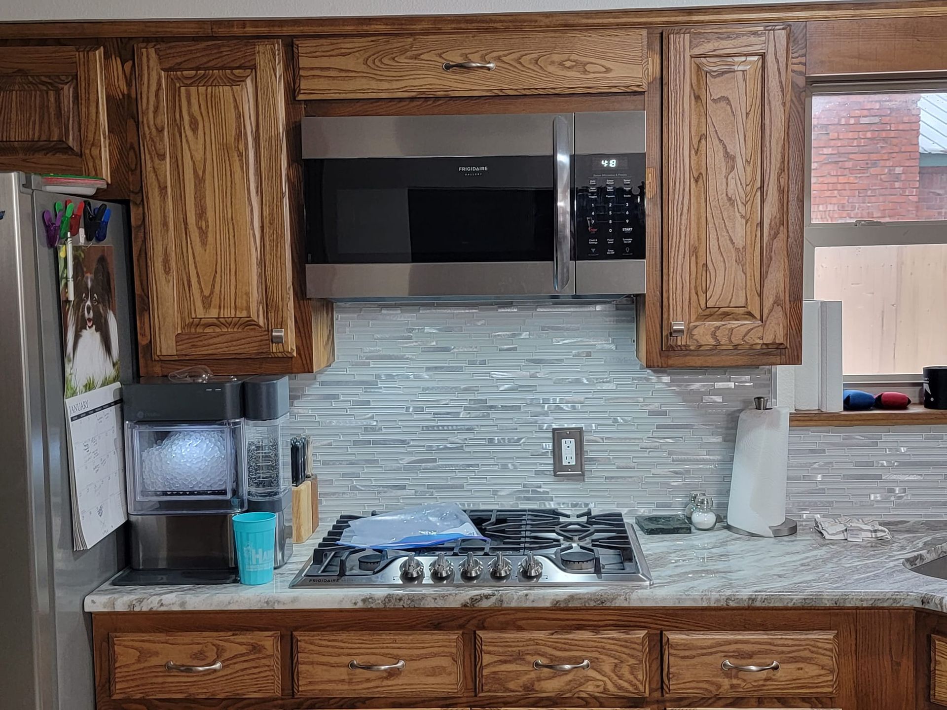 A kitchen with wooden cabinets , stainless steel appliances , a stove , microwave and refrigerator.