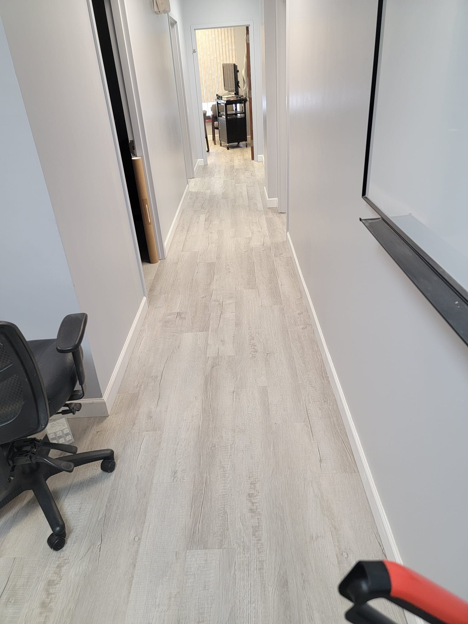 A long hallway with a chair and a white board on the wall.