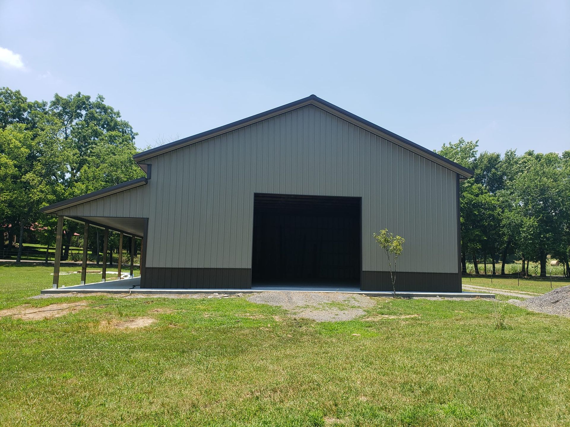 A large metal barn is sitting in the middle of a grassy field.