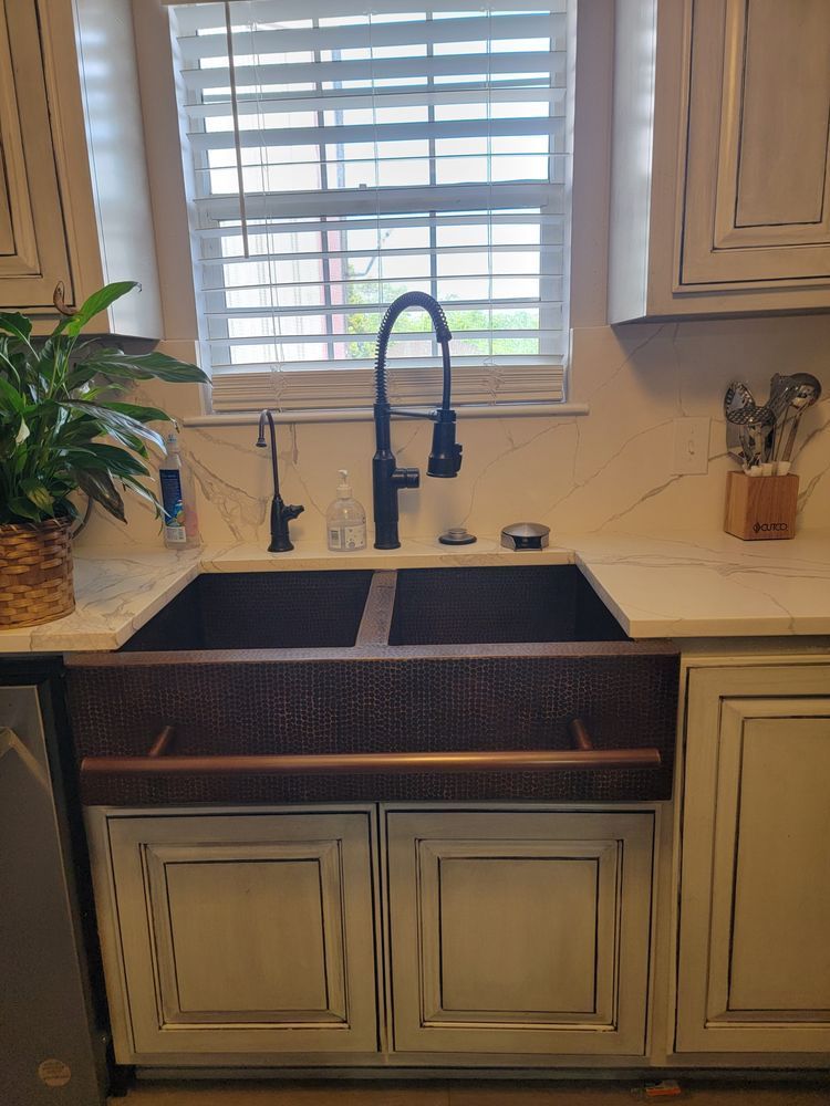 Copper farmhouse sink with a black faucet and window above.