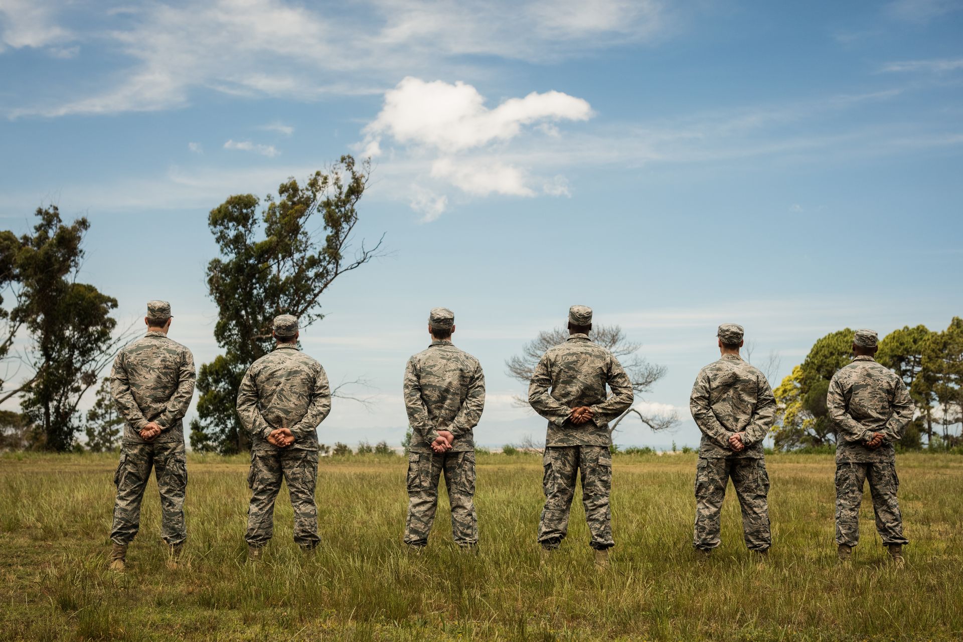A group of soldiers are standing in a field with their hands behind their backs.