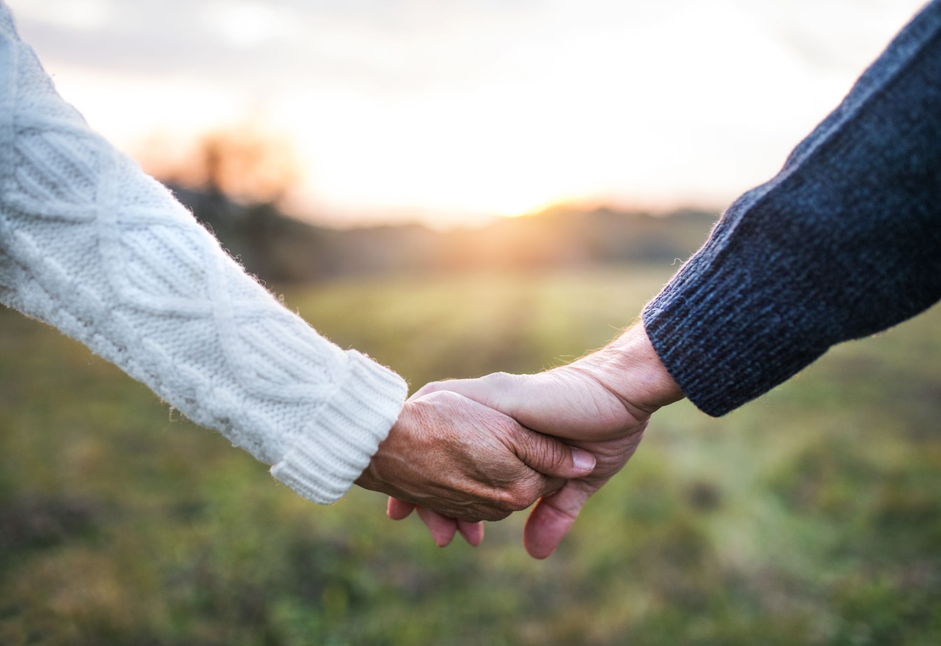 Two people holding hands in a field during sunset, wearing cozy sweaters.