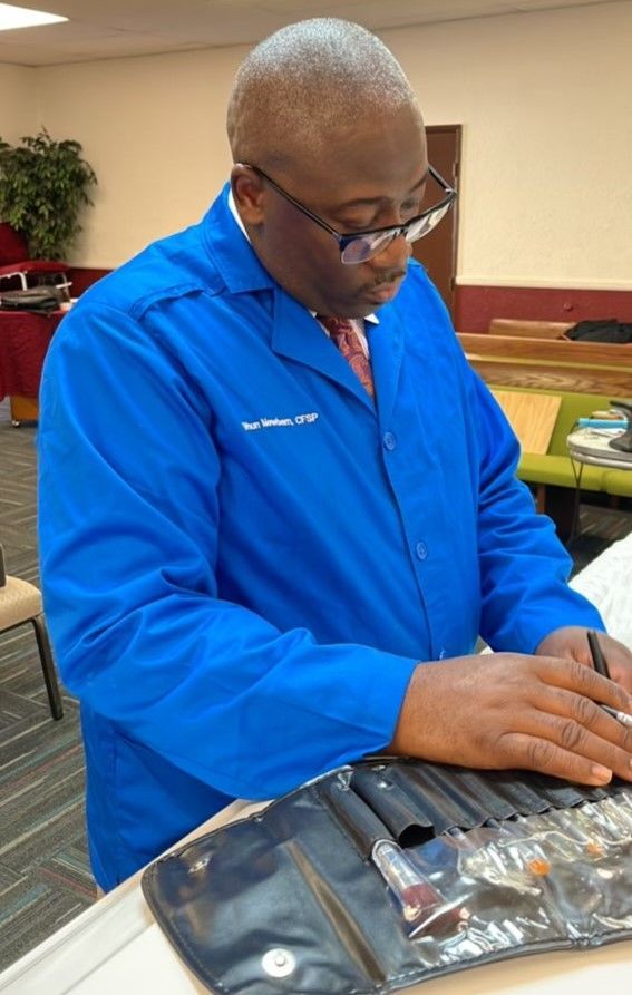 A person wearing a blue coat selects a tool from a makeup brush kit on a table in an indoor setting.
