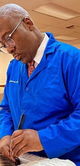 A professional in a blue medical coat examines a patient's ear with a diagnostic tool in an indoor office setting.